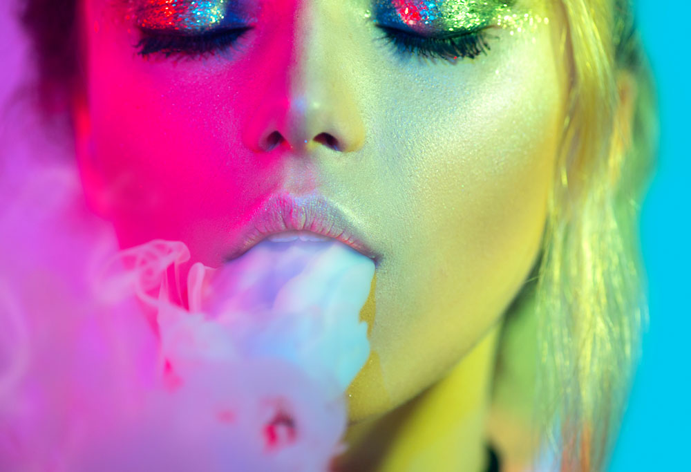 Woman vaping showing large clouds of smoke on a colourful background.